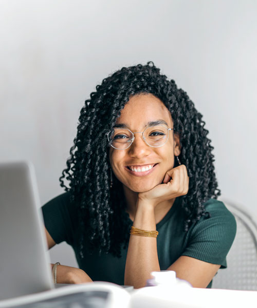 a girl smiling for the camera with a laptop in front of her