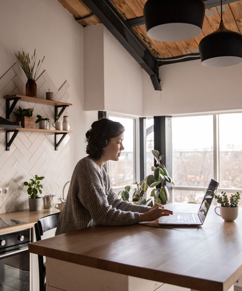 Woman seen sitting at the kitchen counter, typing on her laptop.